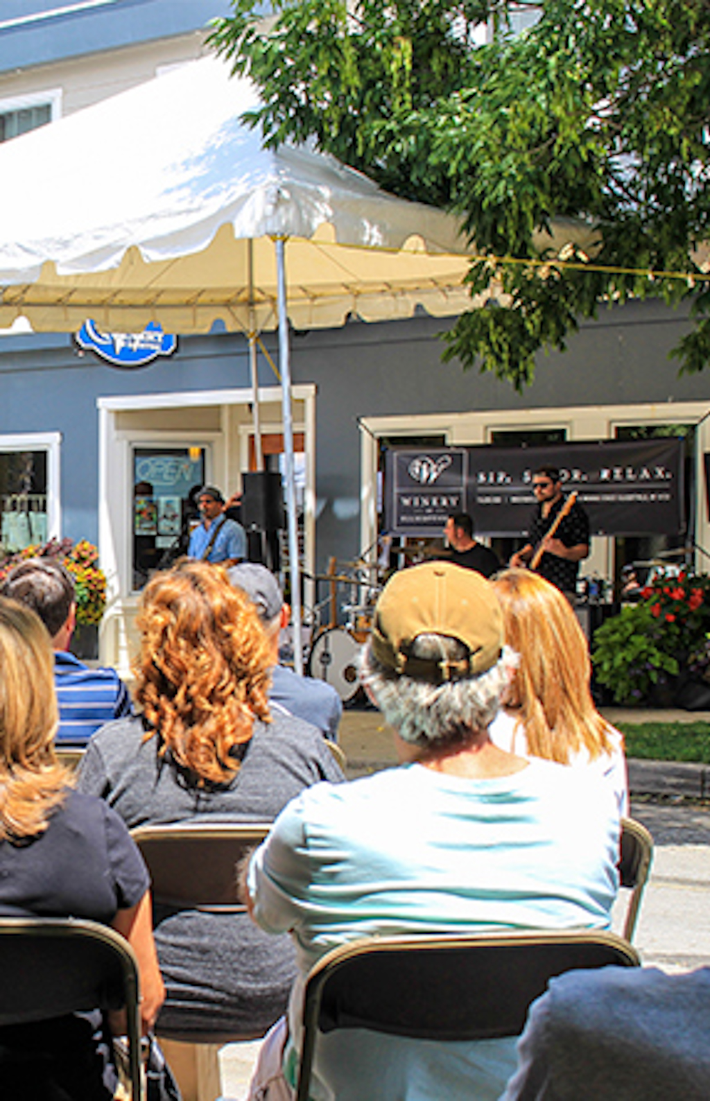 A crowd sits and listens to music being played outside in downtown Ellicottville on a summer day.